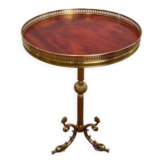 A round, neoclassical-style brass side table with a base decorated with dolphins and a red celluloid top encircled by an openwork gallery, attributed to the House of Jansen.