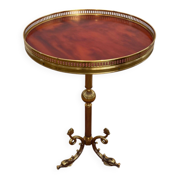 Guéridon rond de style néoclassique en laiton à piètement décoré de dauphins et plateau de celluloïde rouge cerclé d'une gallerie ajourée attribué à la Maison Jansen