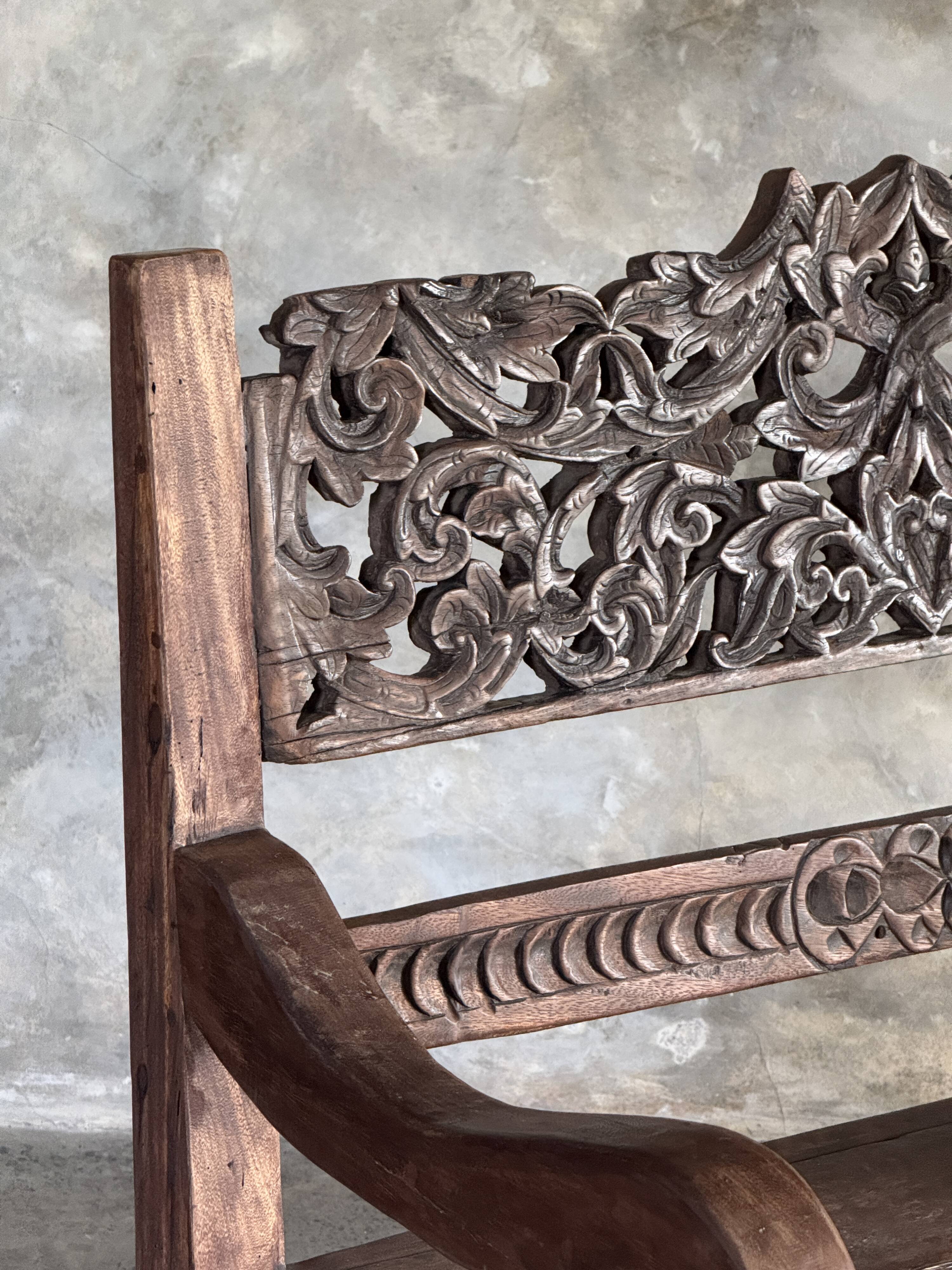 Small antique Indonesian bench in carved teak with plant and floral motifs.