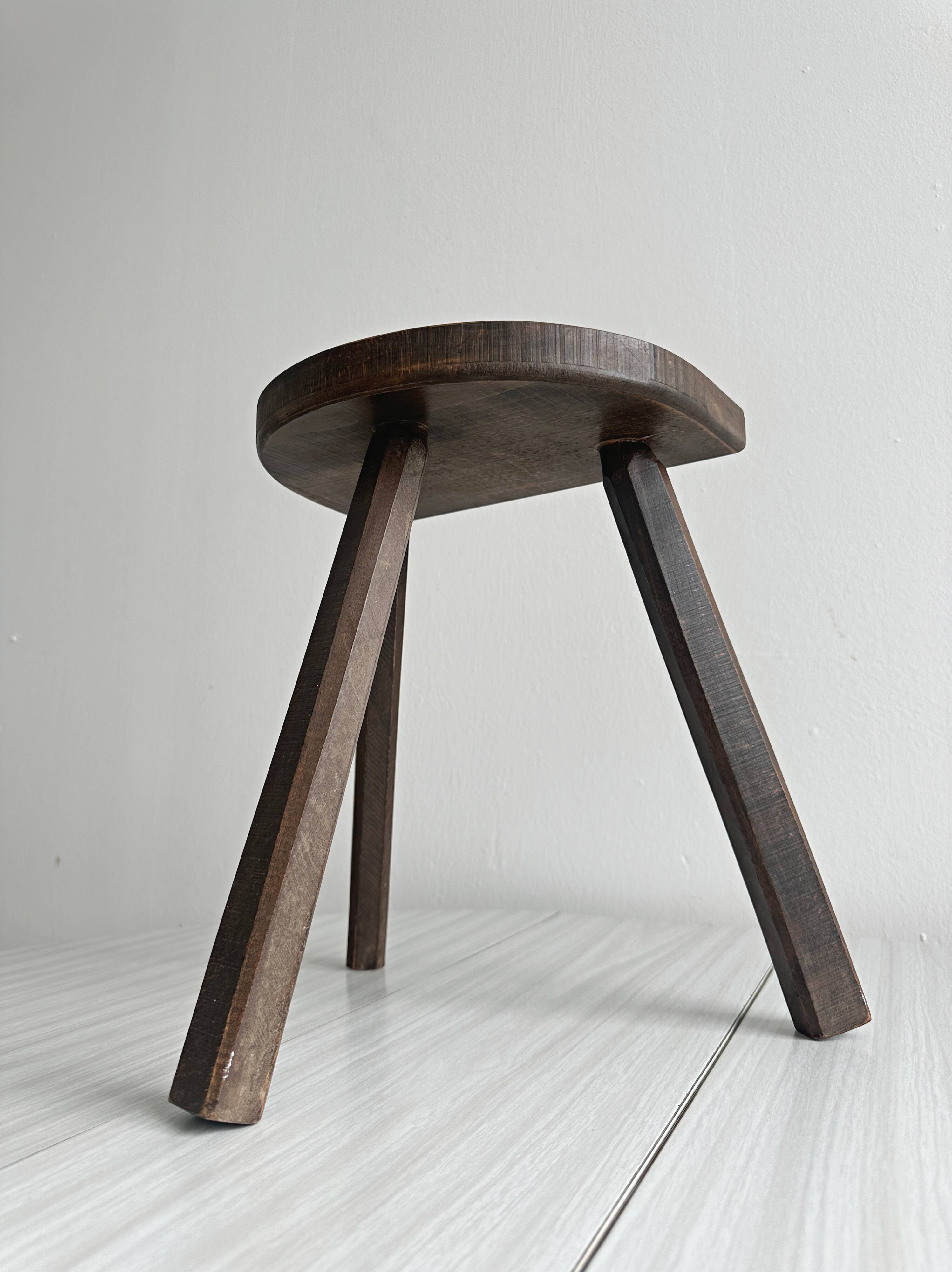 Antique wooden tripod stool with a semi-circular seat.