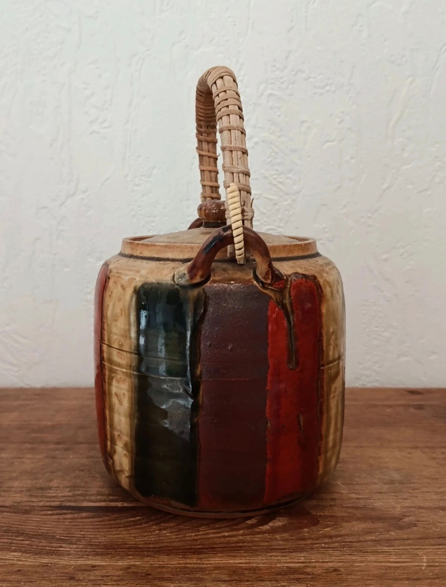 Vintage ceramic teapot with an enamel finish, rattan handle, warm tones.
