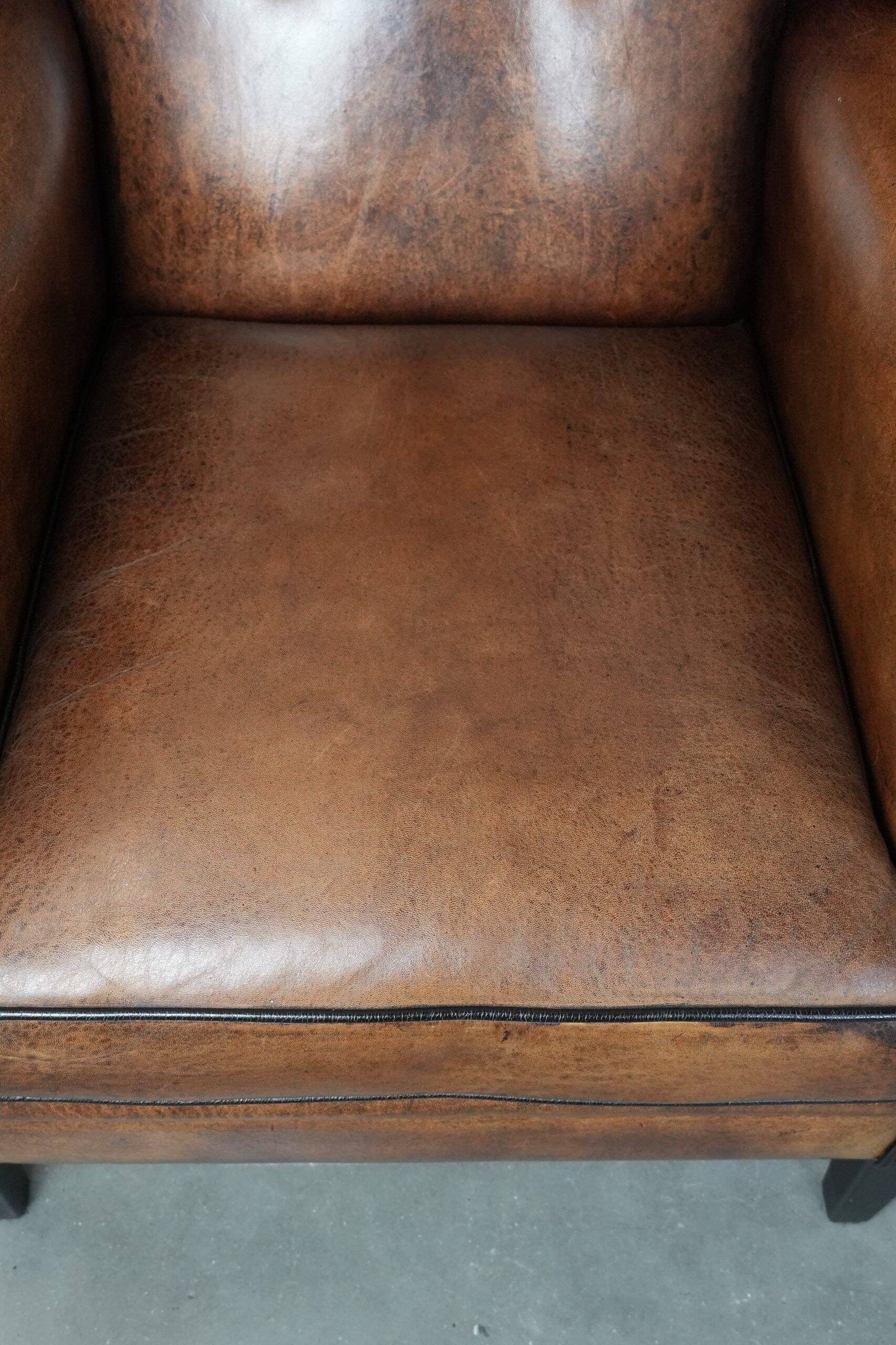 Sheepskin wingback armchair with decorative nails and black piping