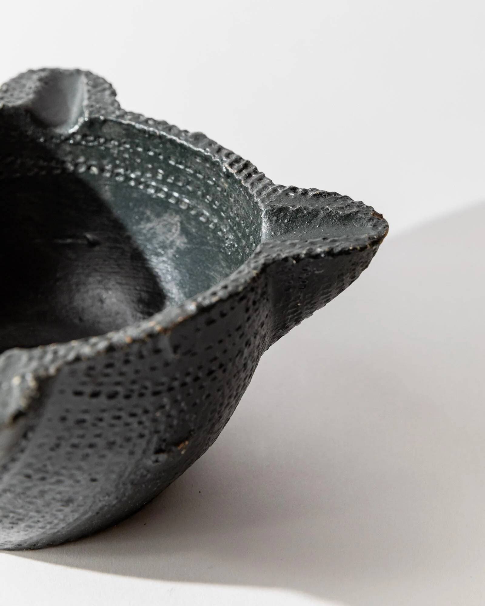 Vintage ceramic ashtray from the 1960s, black, hand-sculpted texture, organic shape.