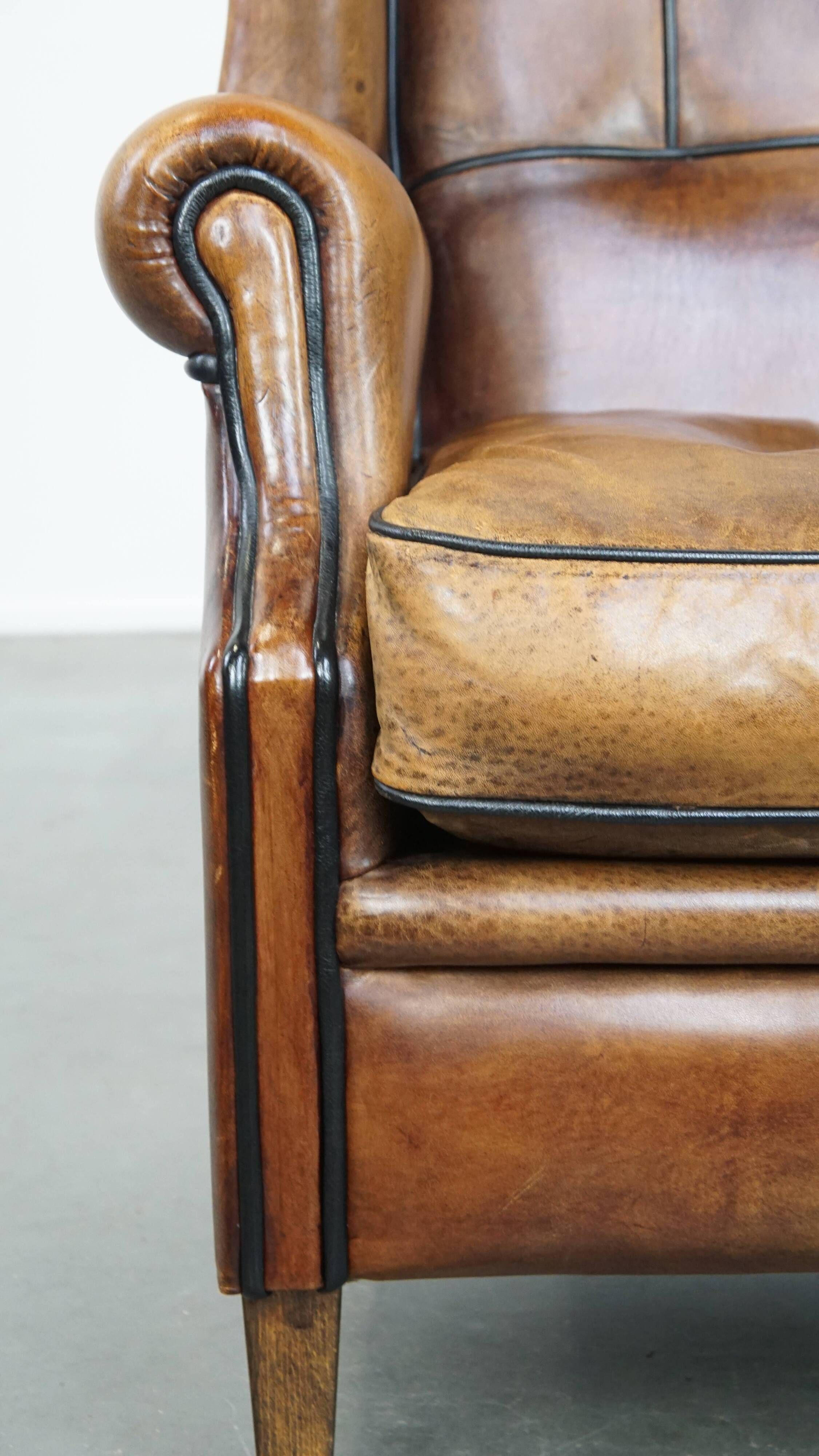 Cognac-colored sheep leather wingback chair finished with black piping