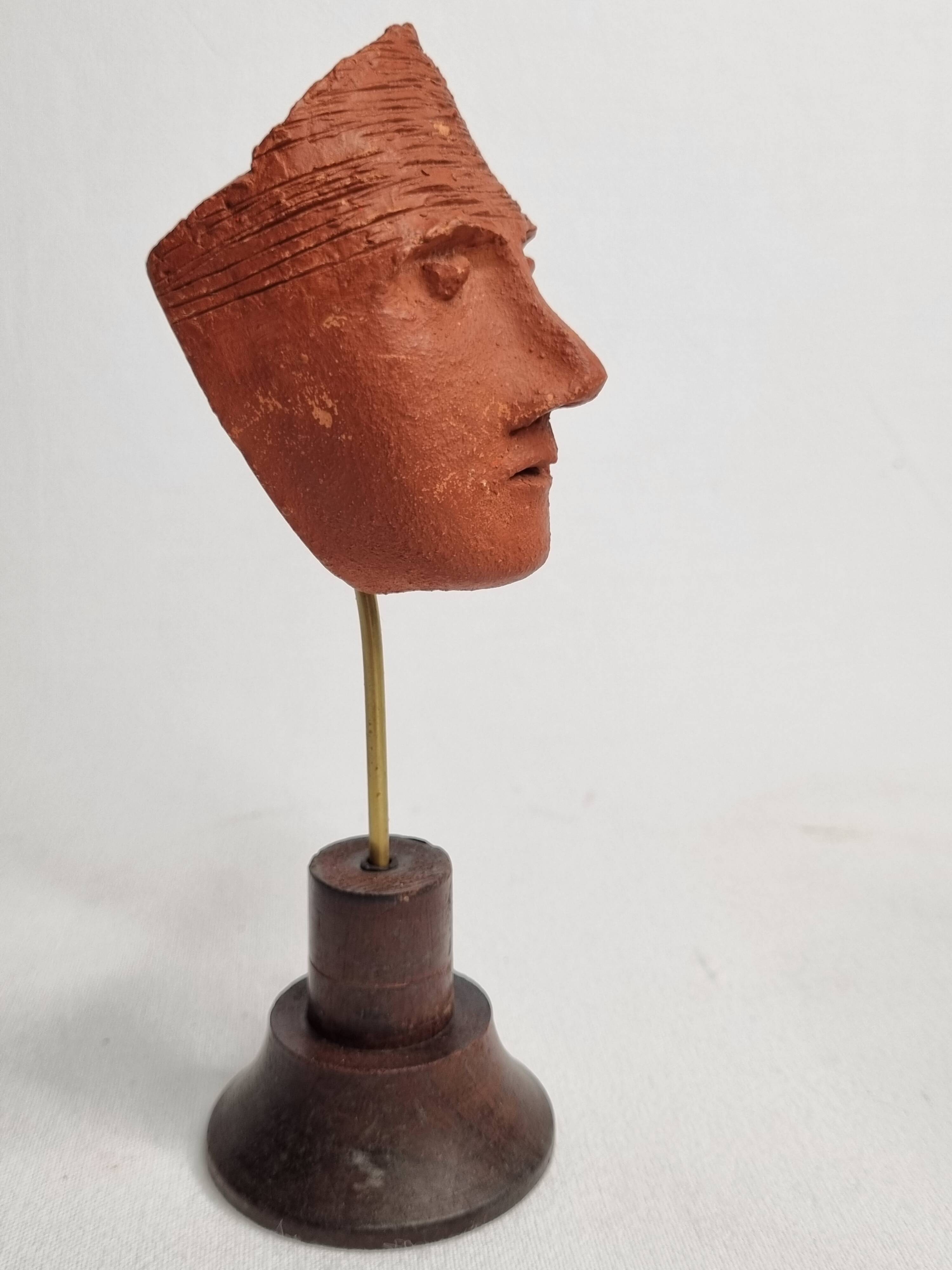 Stylized head in patinated ochre terracotta on a dark wooden base, 17 cm