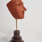 Stylized head in patinated ochre terracotta on a dark wooden base, 17 cm