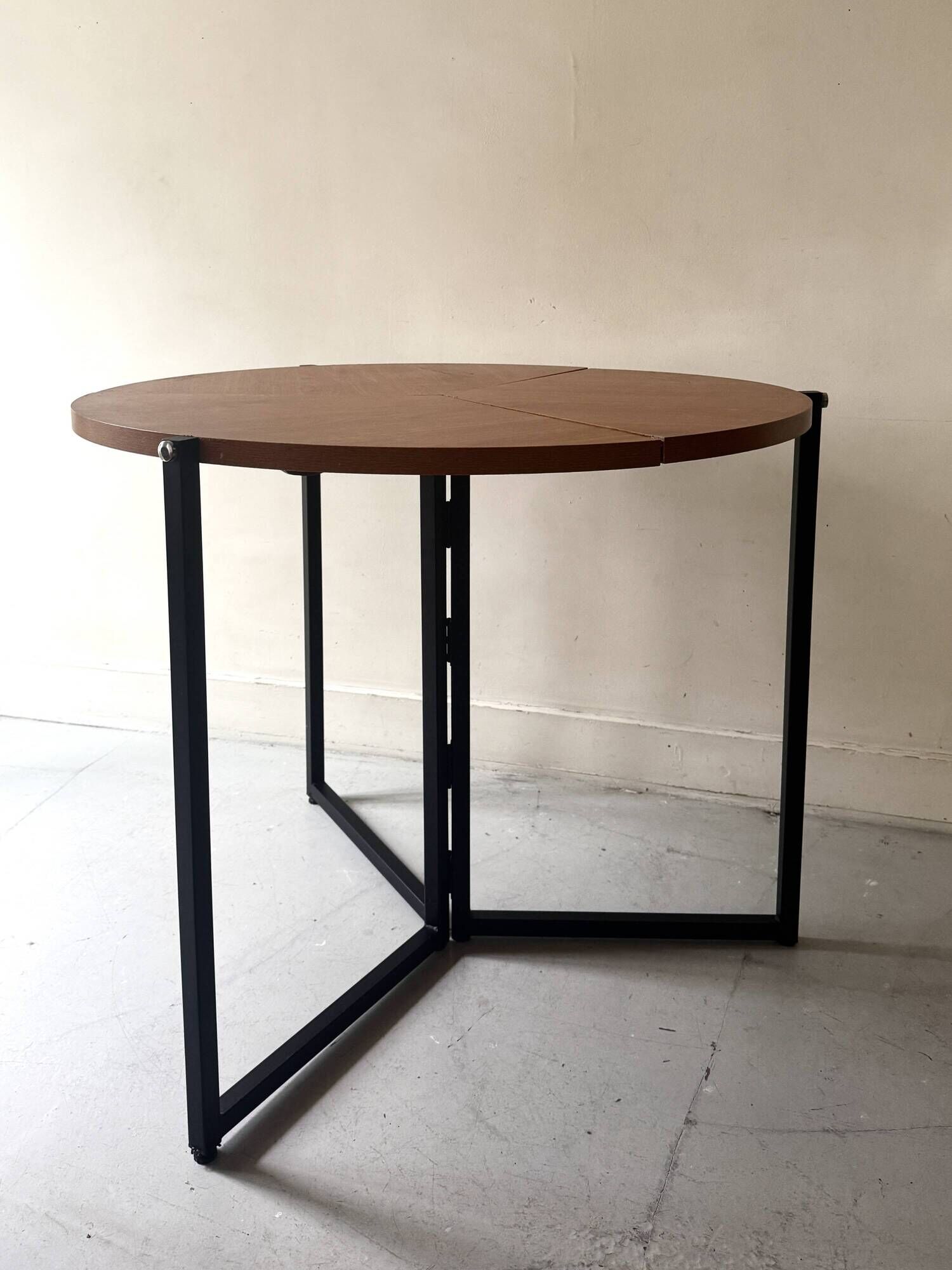 Modernist round folding dining table in wood and metal.