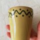 Mustard-colored ceramic cup or glass with green decor