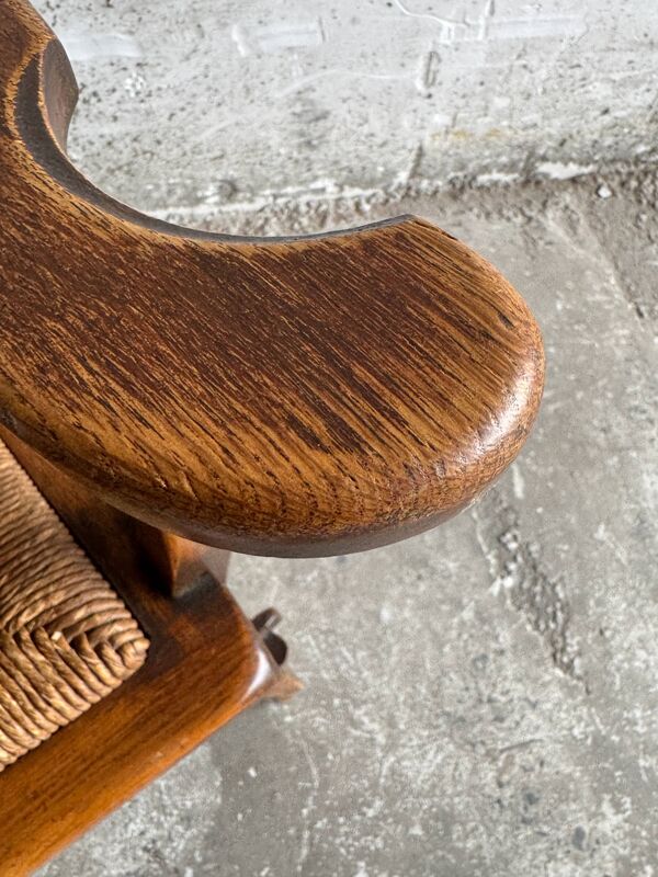 Fauteuil brutaliste en bois massif brun foncé avec assise en rotin naturel et dossier en cuir cognac