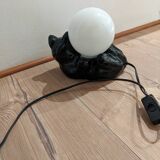 Black cat playing with its globe table lamp