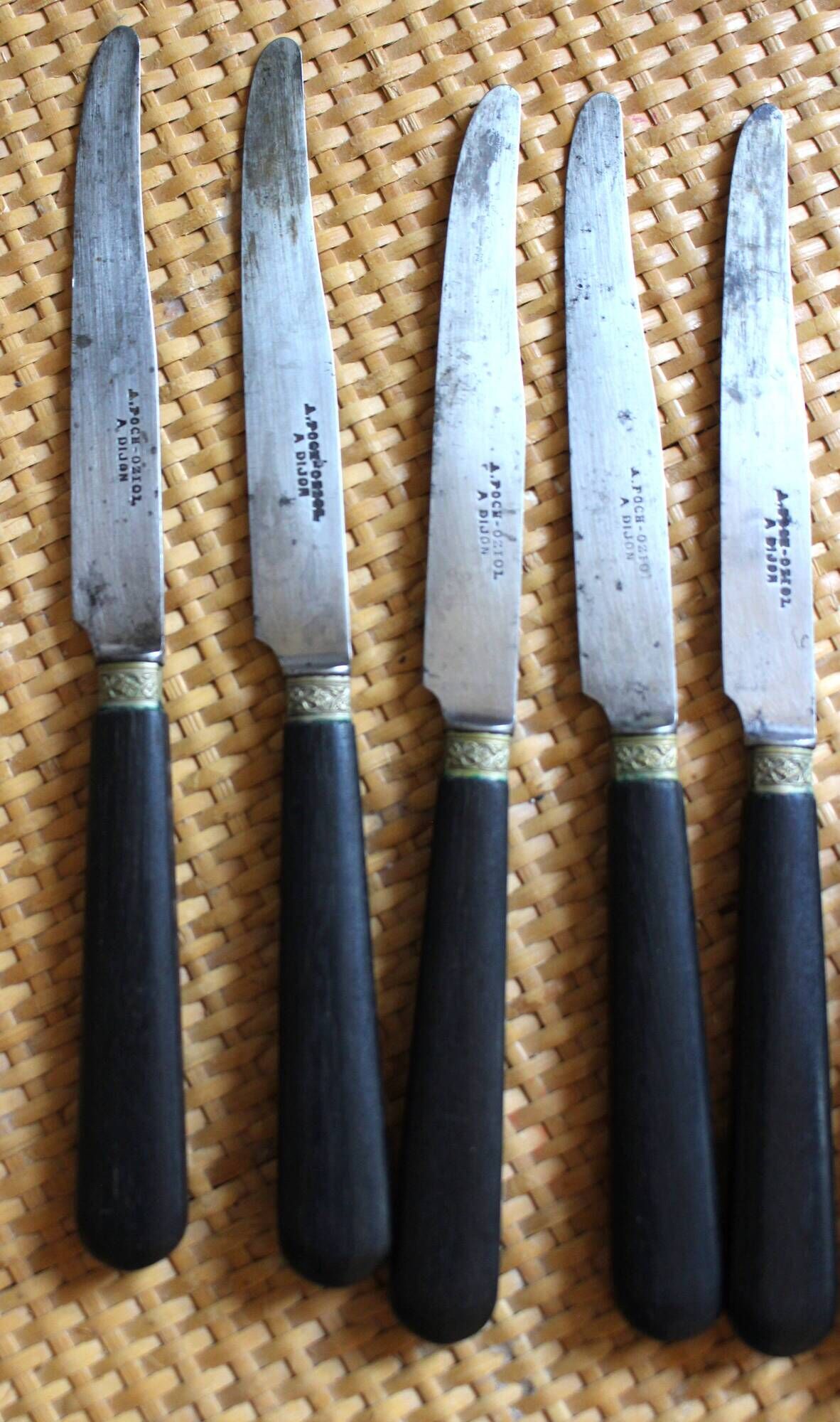 A set of 8 knives with black wooden handles and bolsters.