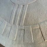 Round ecru rug with geometric relief patterns in wool