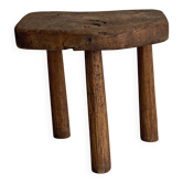 Antique three-legged stool made of raw solid wood.
