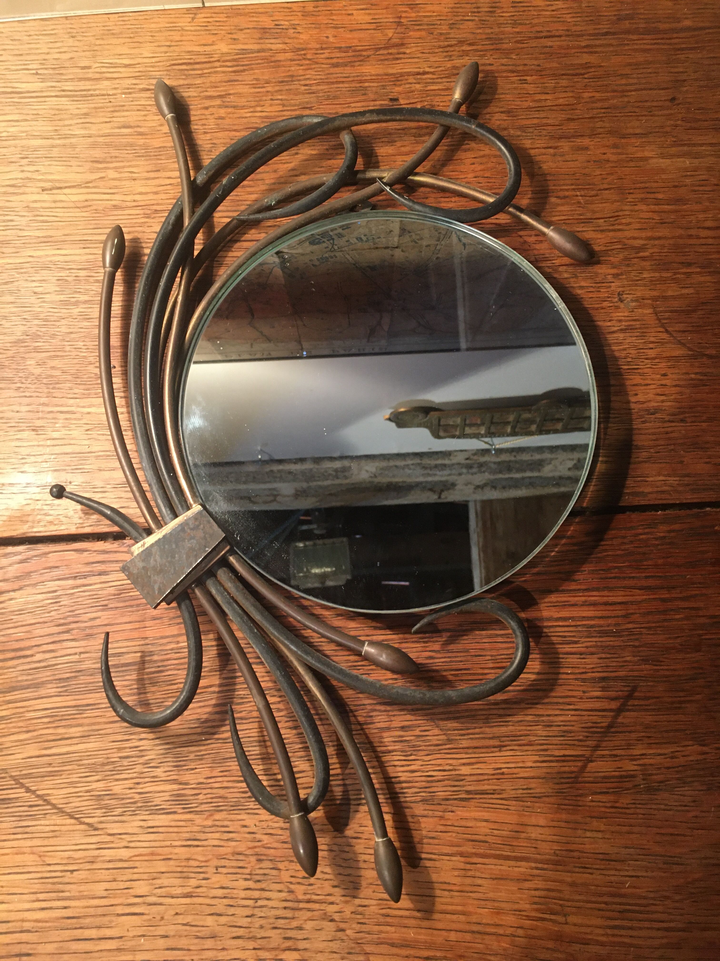 Round mirror surrounded by art deco style metal plants