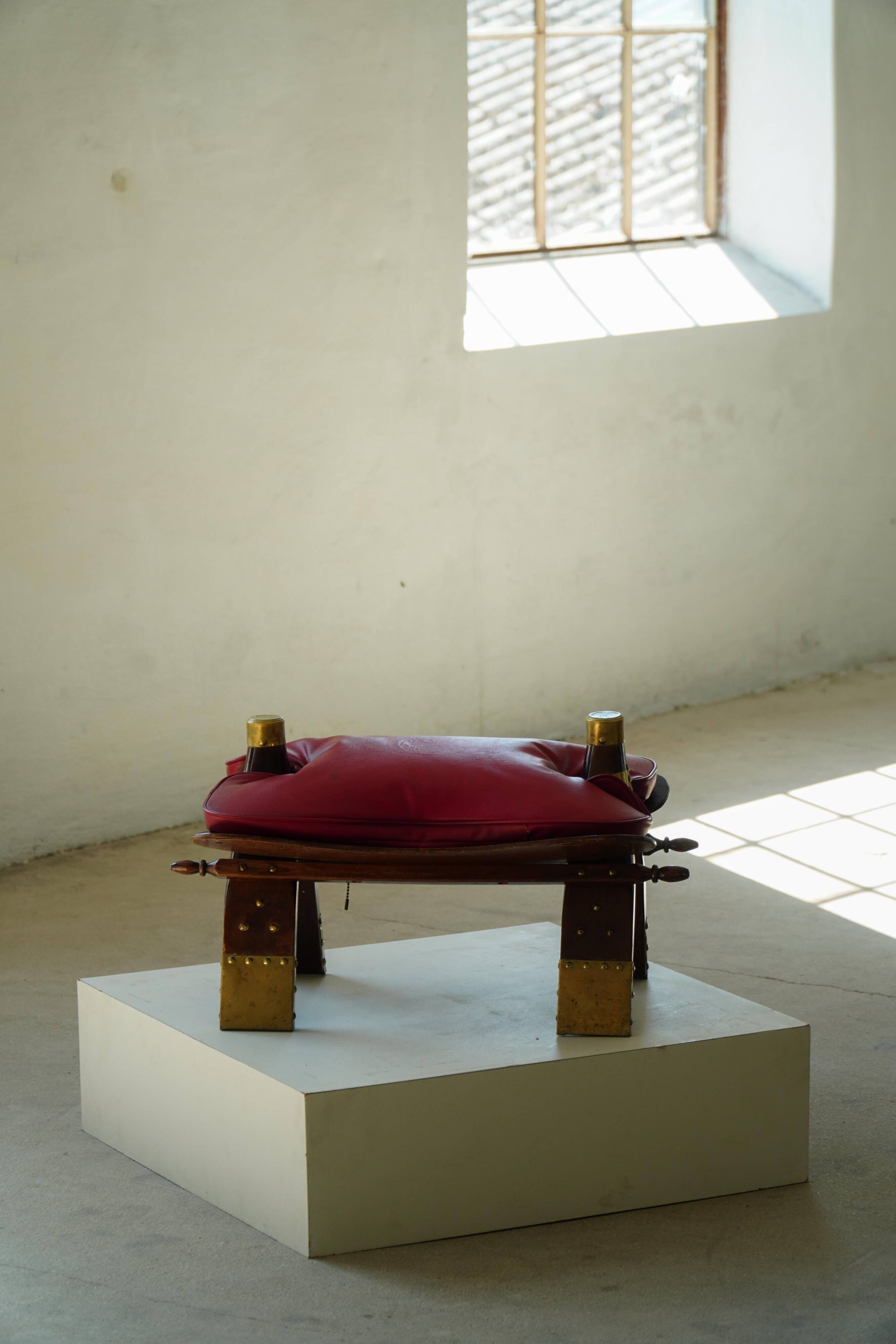 Moroccan stool in the shape of a camel saddle, stained wood, brass and leather, North Africa, 1980.