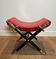 Neoclassical curule stool in red leather, decorated with crossed swords in bronze and metal covered in black leather.