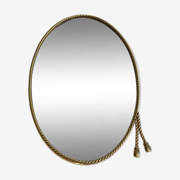 Oval brass mirror surrounded by a cord and adorned