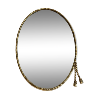 Oval brass mirror surrounded by a cord and adorned