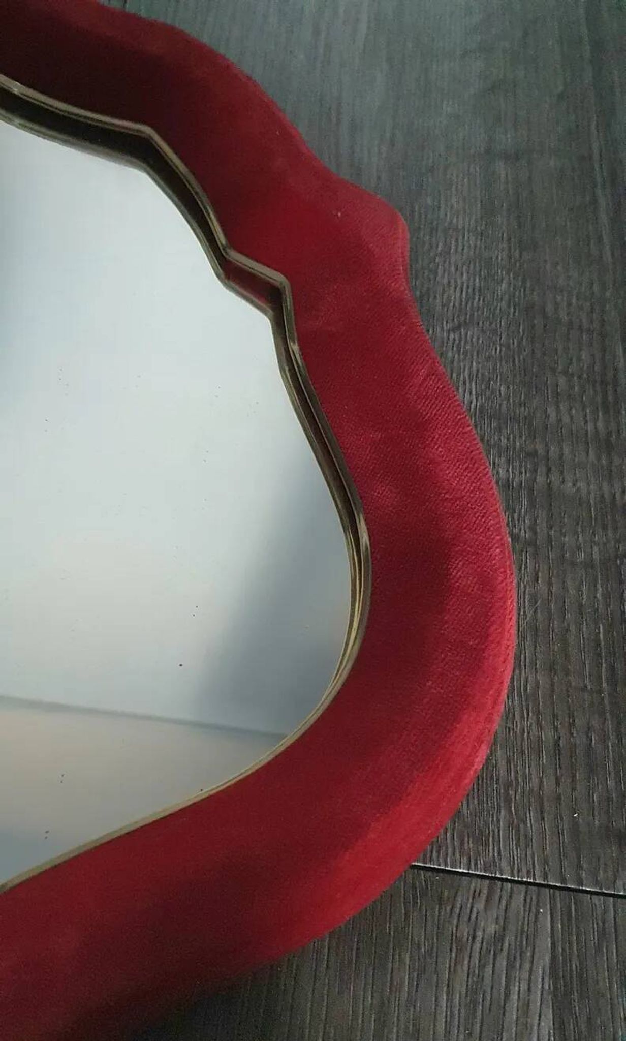 Vintage mirror with a scalloped shape in burgundy velvet and a golden trim.
