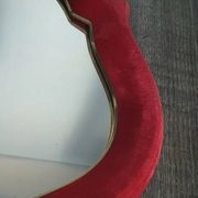 Vintage mirror with a scalloped shape in burgundy velvet and a golden trim.