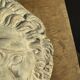 Off-white plaster lion head relief on natural wood panel — Walter De Buck, classical decorative sculpture