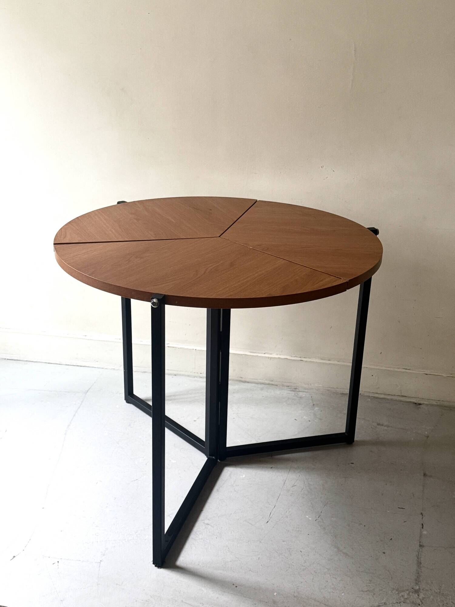 Modernist round folding dining table in wood and metal.