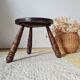 Small brutalist tripod stool made of turned wood.