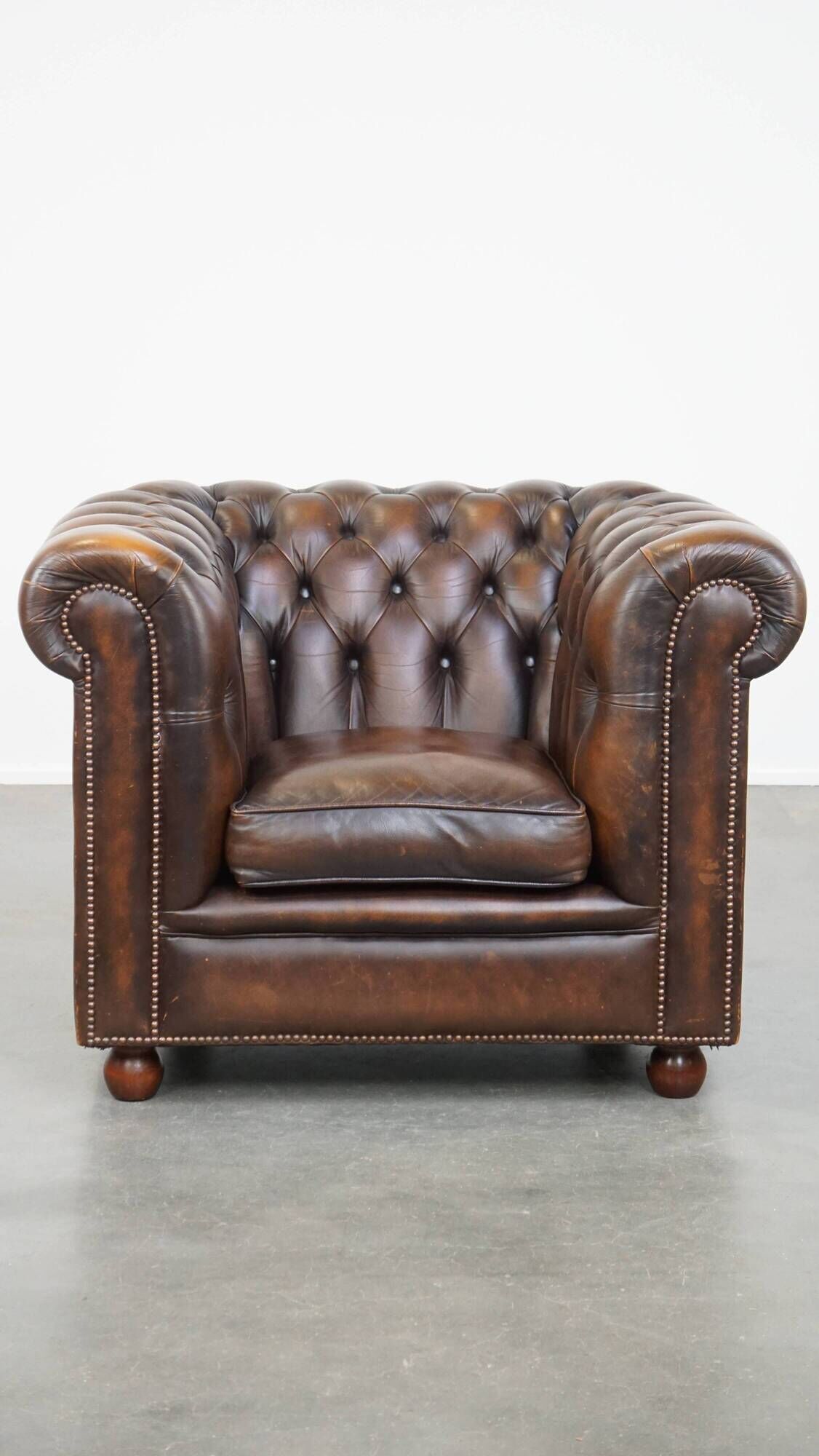 Cowhide English Chesterfield armchair with ball legs and timeless finish