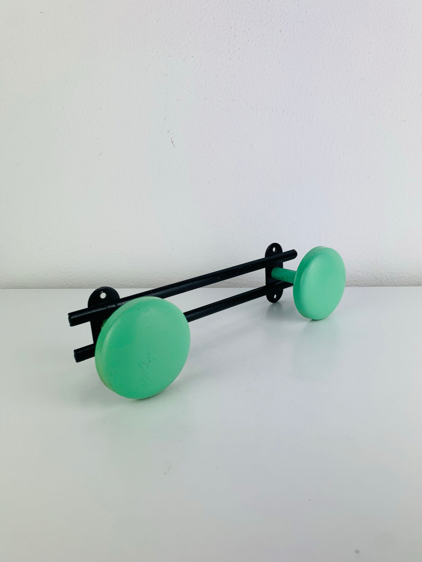 Wall-mounted coat rack with 2 green hooks from the 1950s.