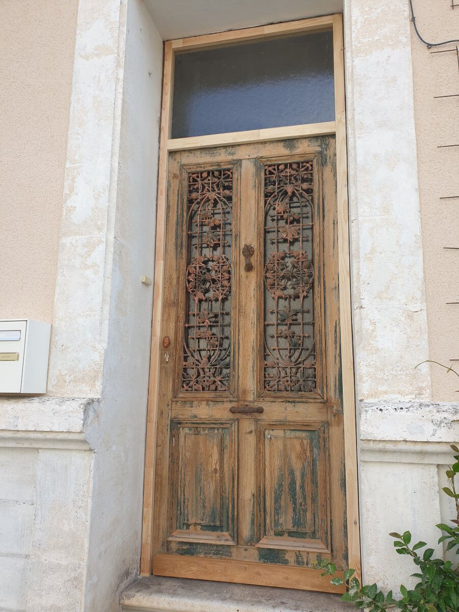 Front door of a house or building in the city centre, with a dolphin door knocker and frame + transom.