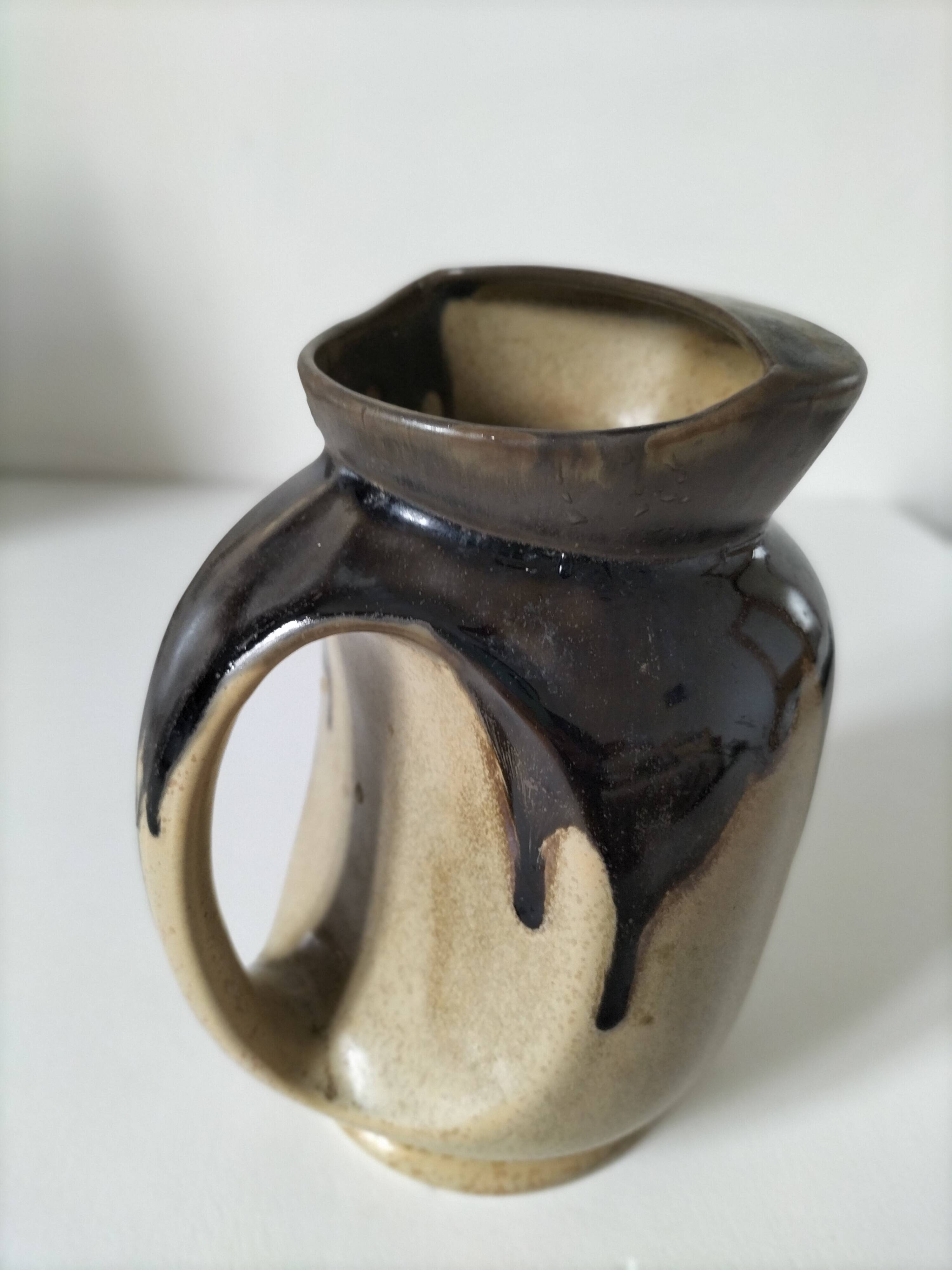 Stoneware jug with deep black drips on a sandy background.