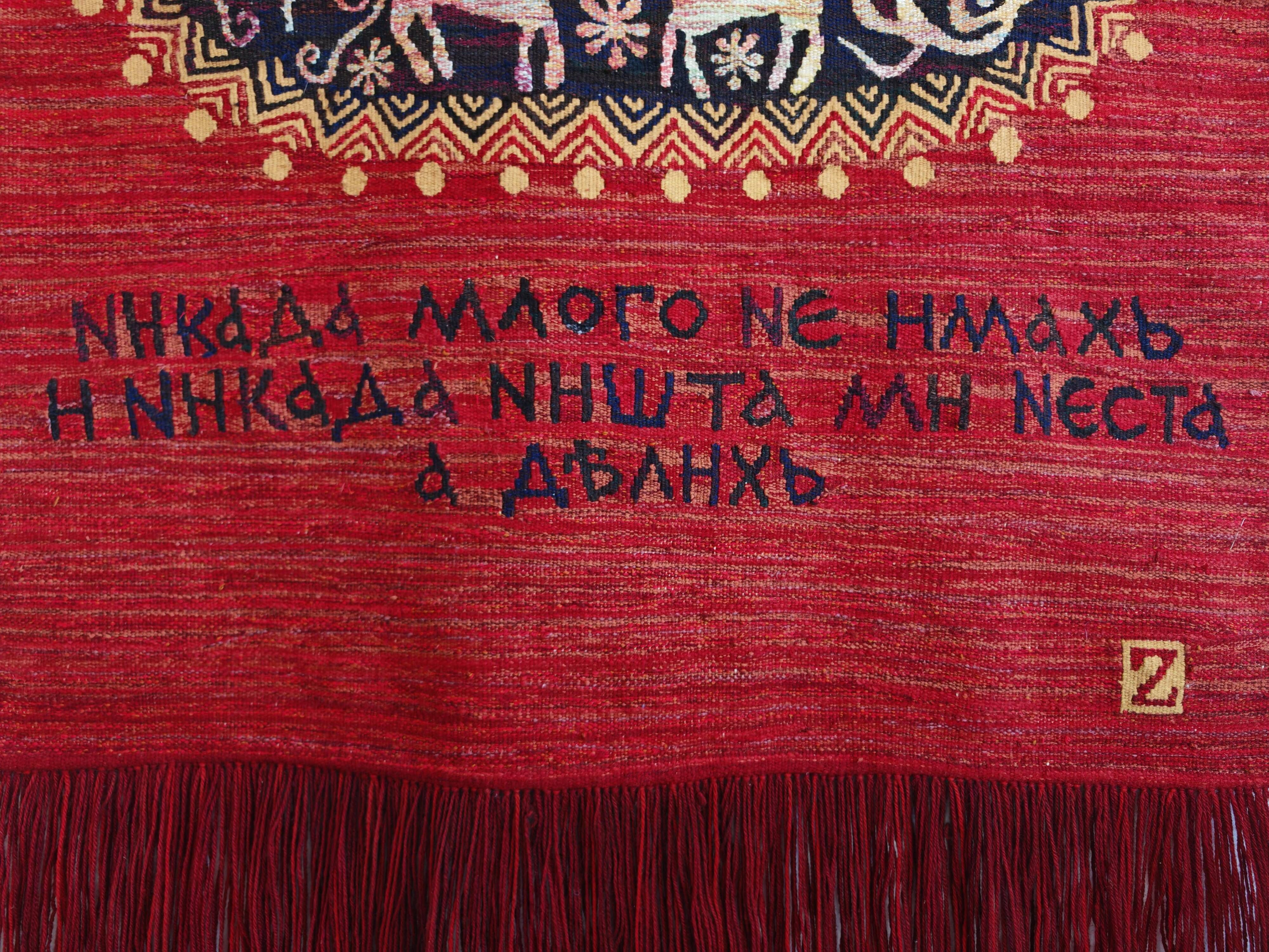 Vintage handwoven tapestry with a folk scene and archaic Slavic writing.