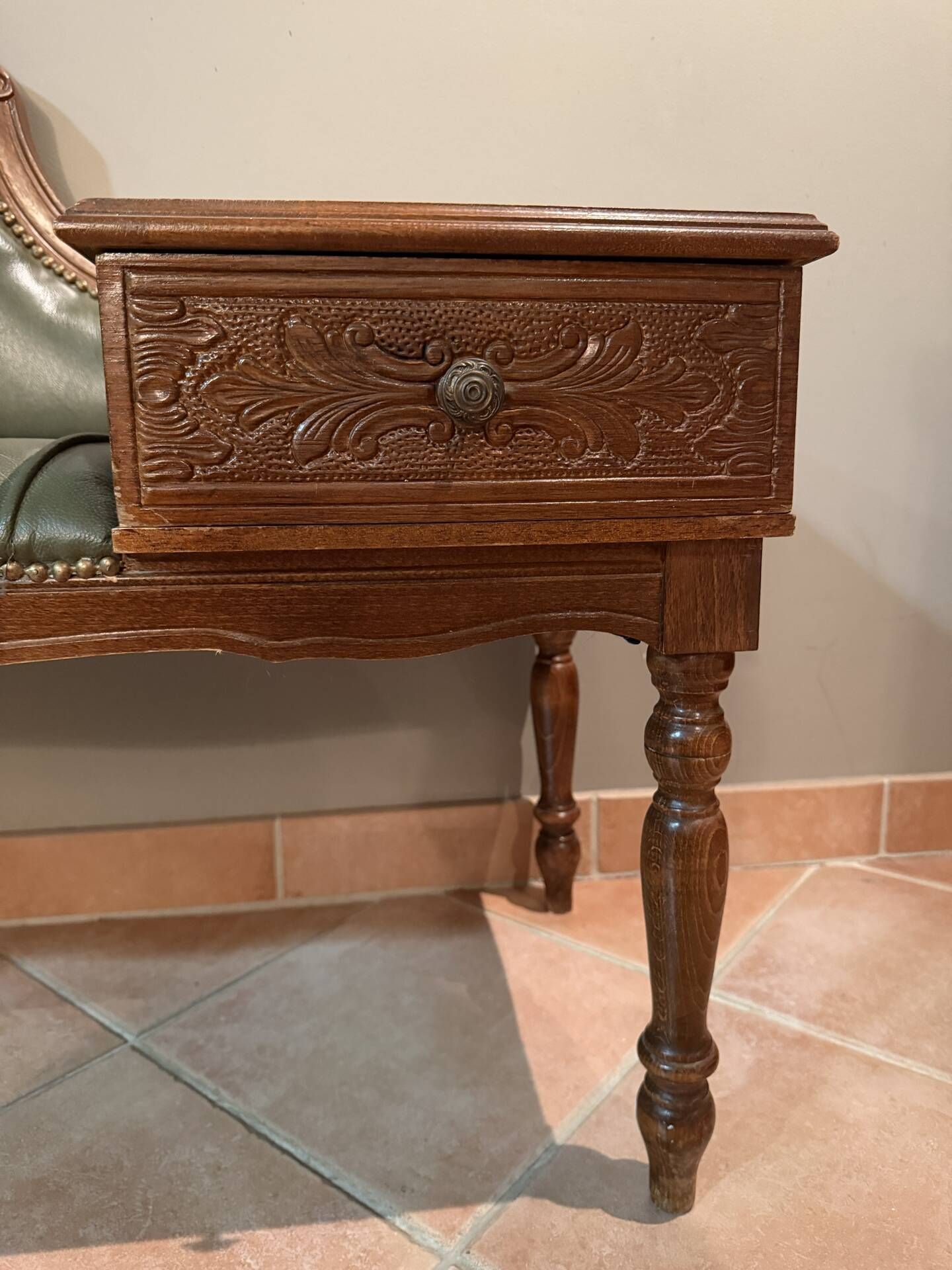 Antique carved wooden bench with green upholstered seat and backrest.