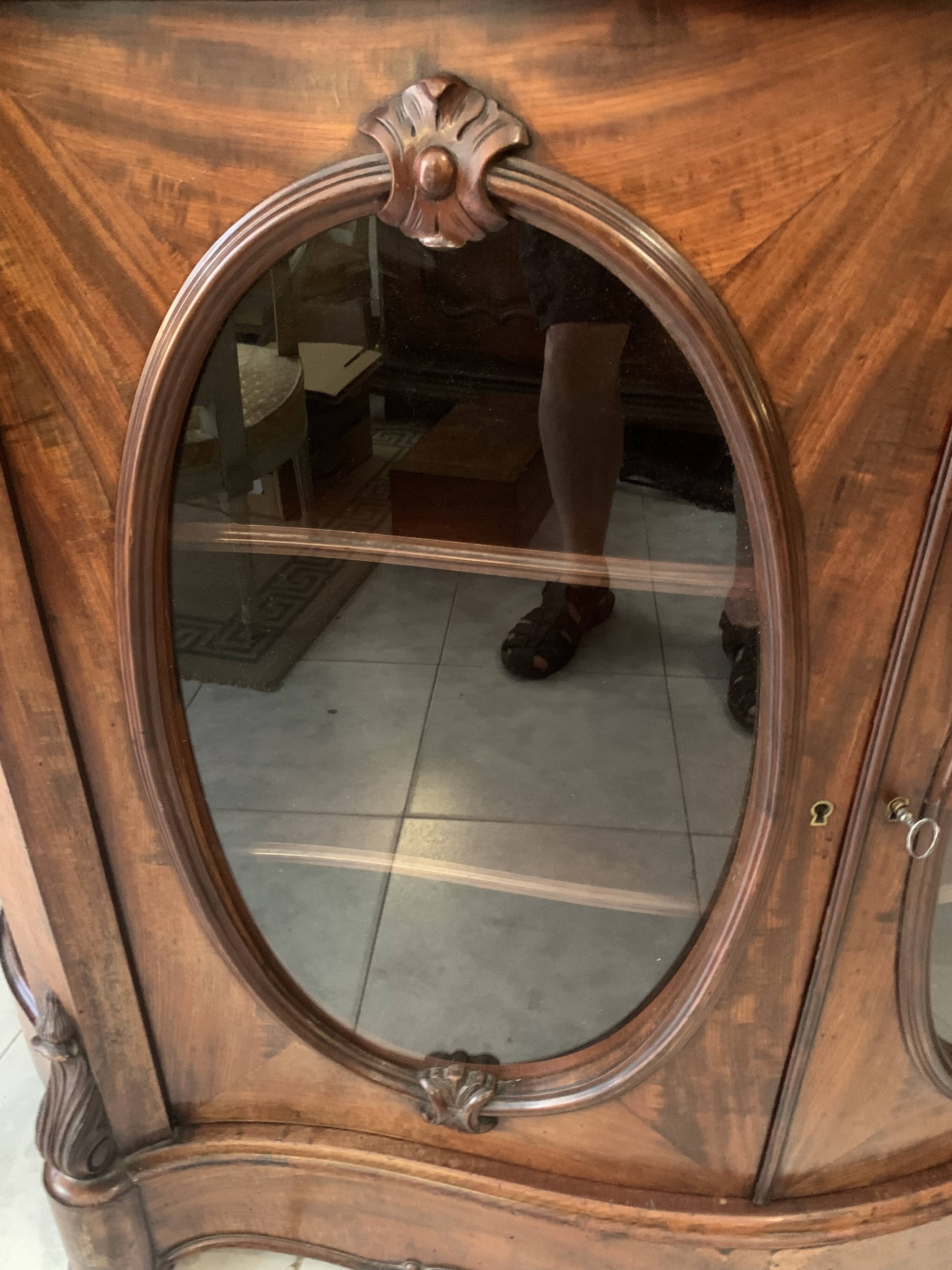 Curved mahogany display cabinet from the Napoleon III period. It has two doors and two shelves.