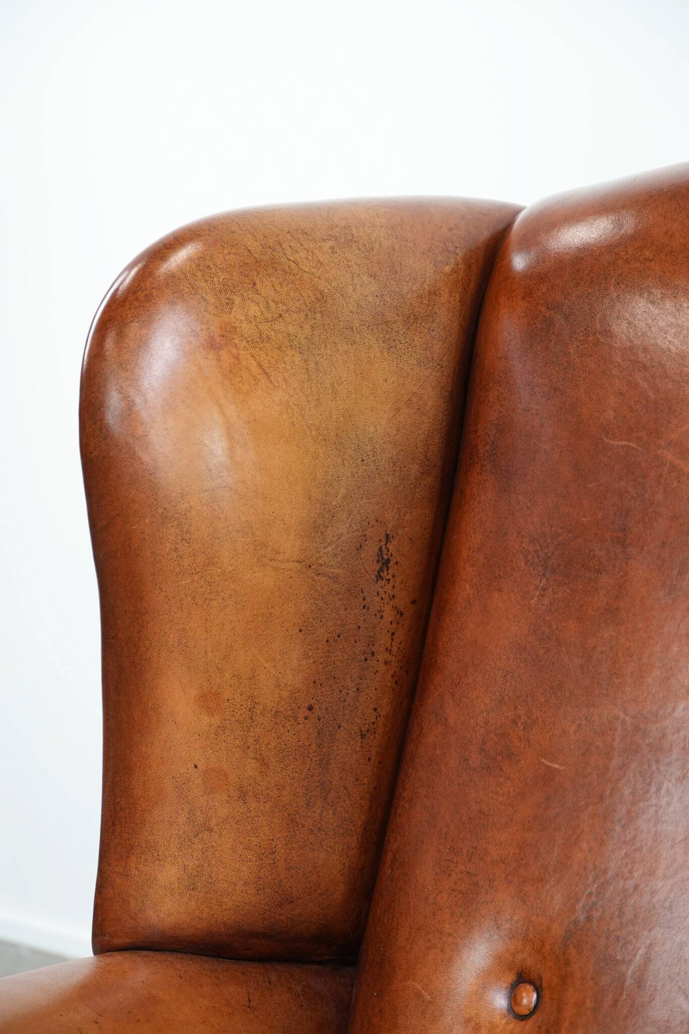 Large sheepskin wingback chair with black piping and decorative nails