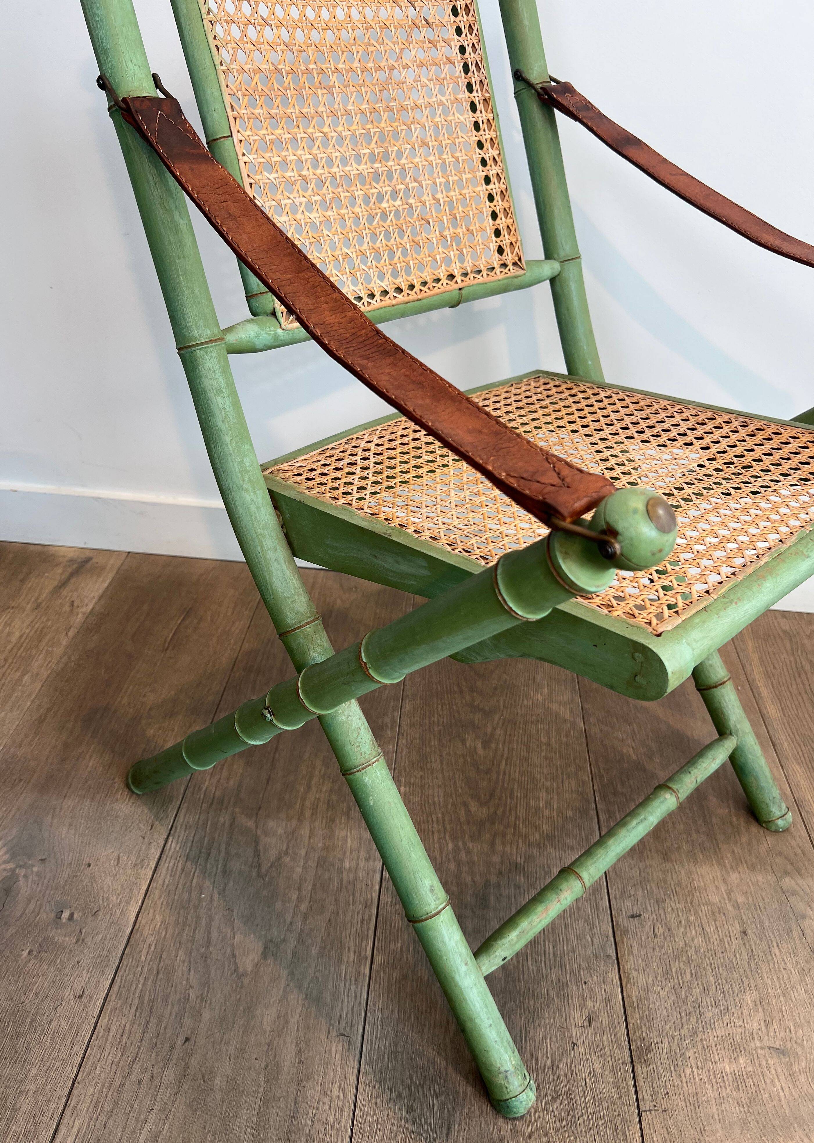 Paire de chaises safari pliantes façon faux-bambou patiné, dossiers et assises cannées et repose-bras en cuir