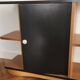 Compact bar cabinet with a pivoting door in black wood.