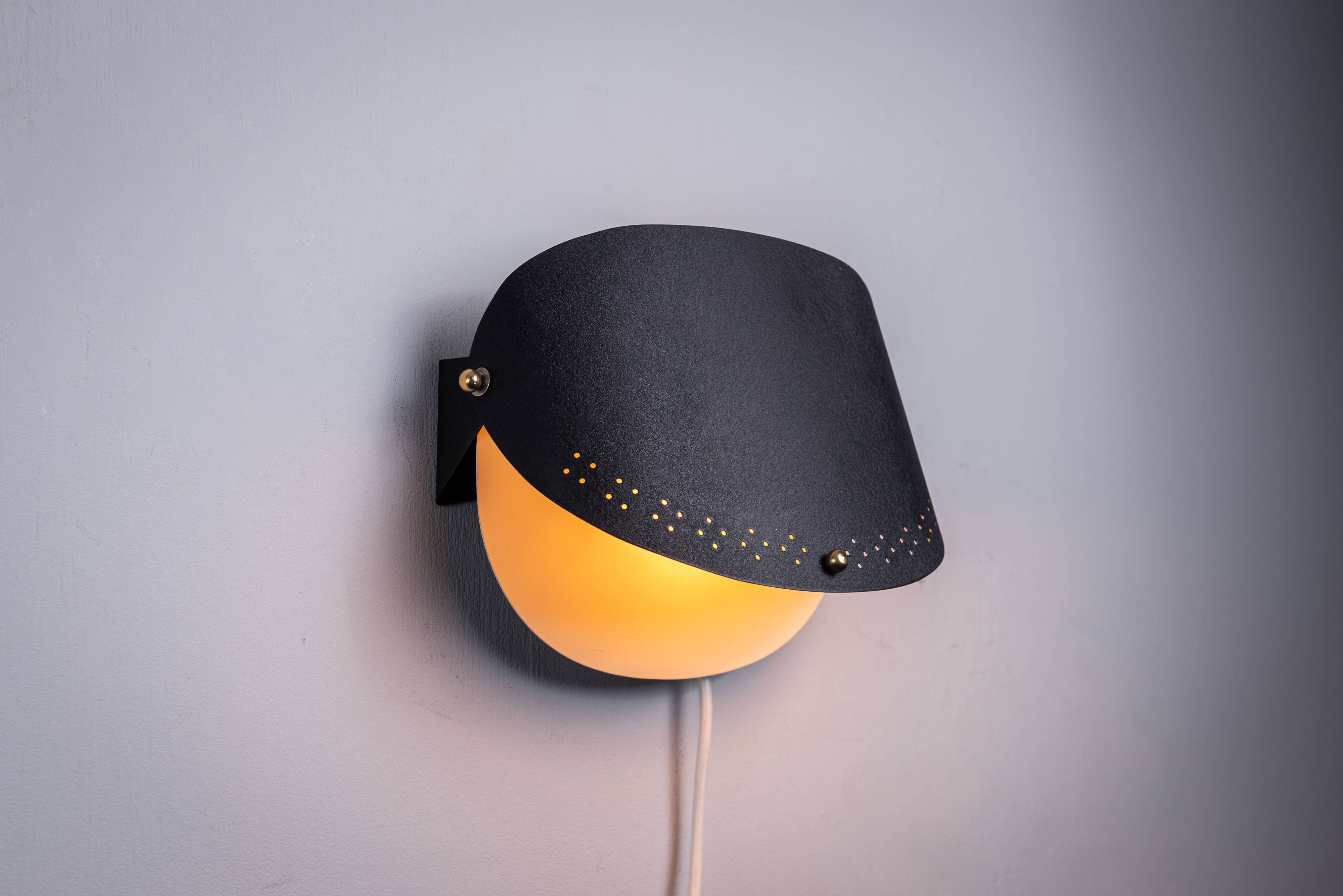 Matte black wall lamps with perforated shades and brass details
