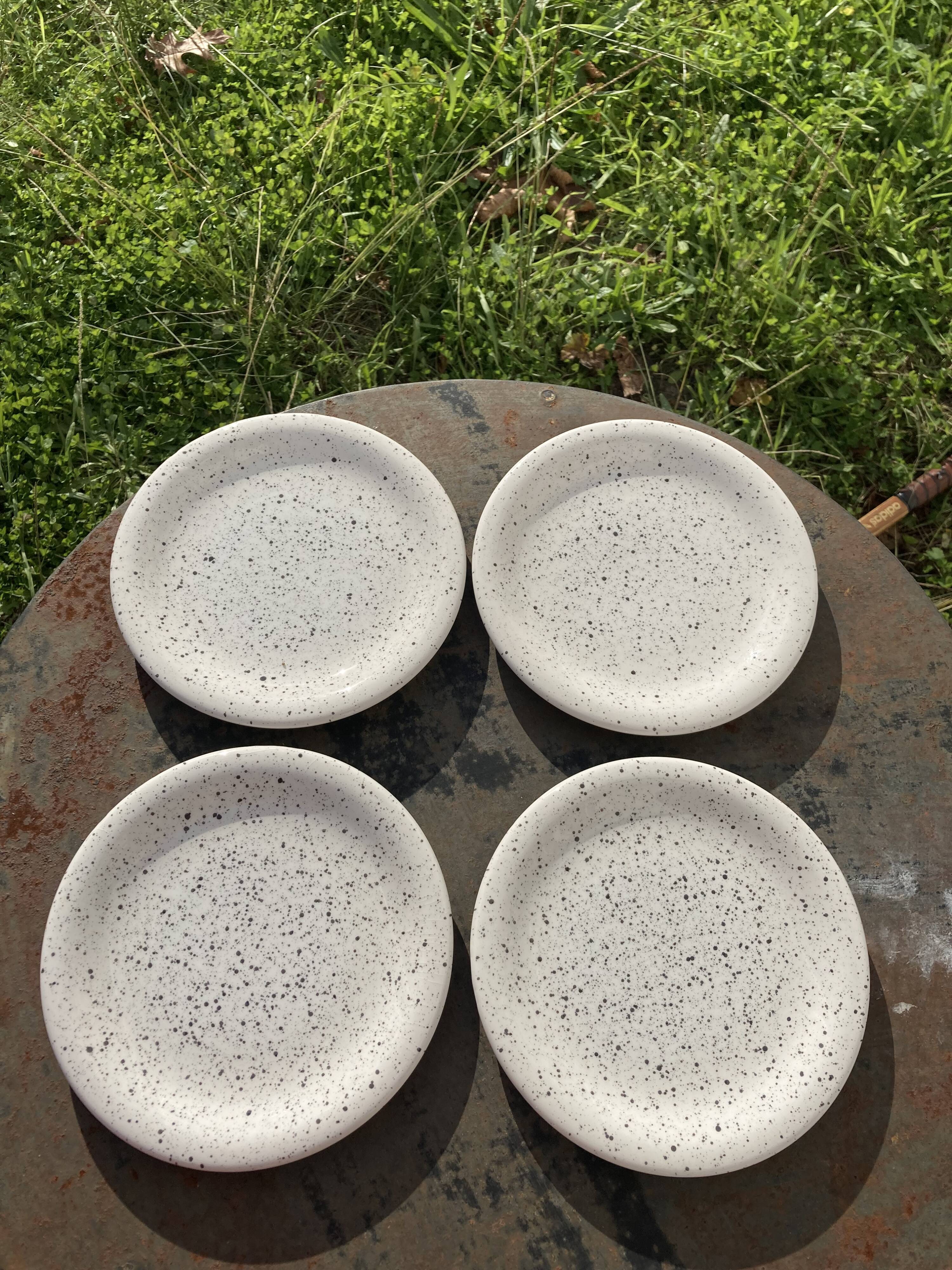 4 black speckled dessert plates on a vintage white background