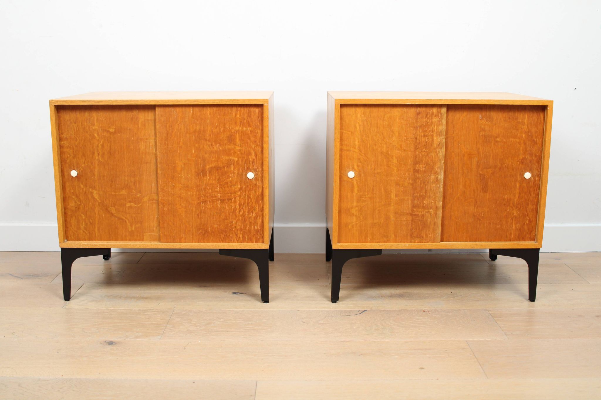 A pair of vintage mid-century bedside tables with oak sliding doors