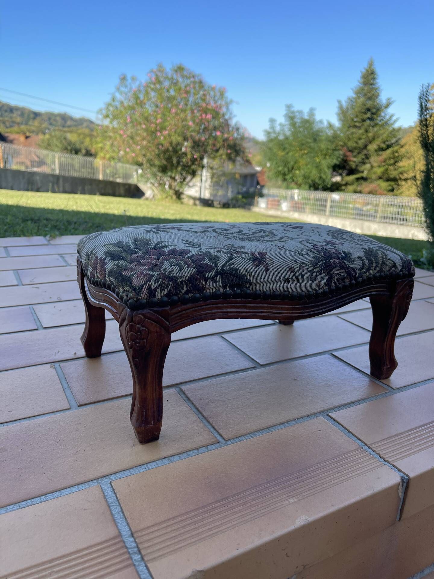 Antique wooden footstool with hand-carved details and floral upholstery –
