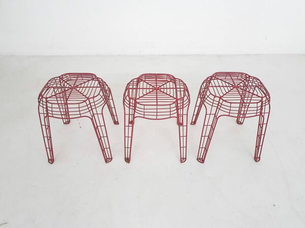 Ensemble de trois tabourets en fil métallique rouge.