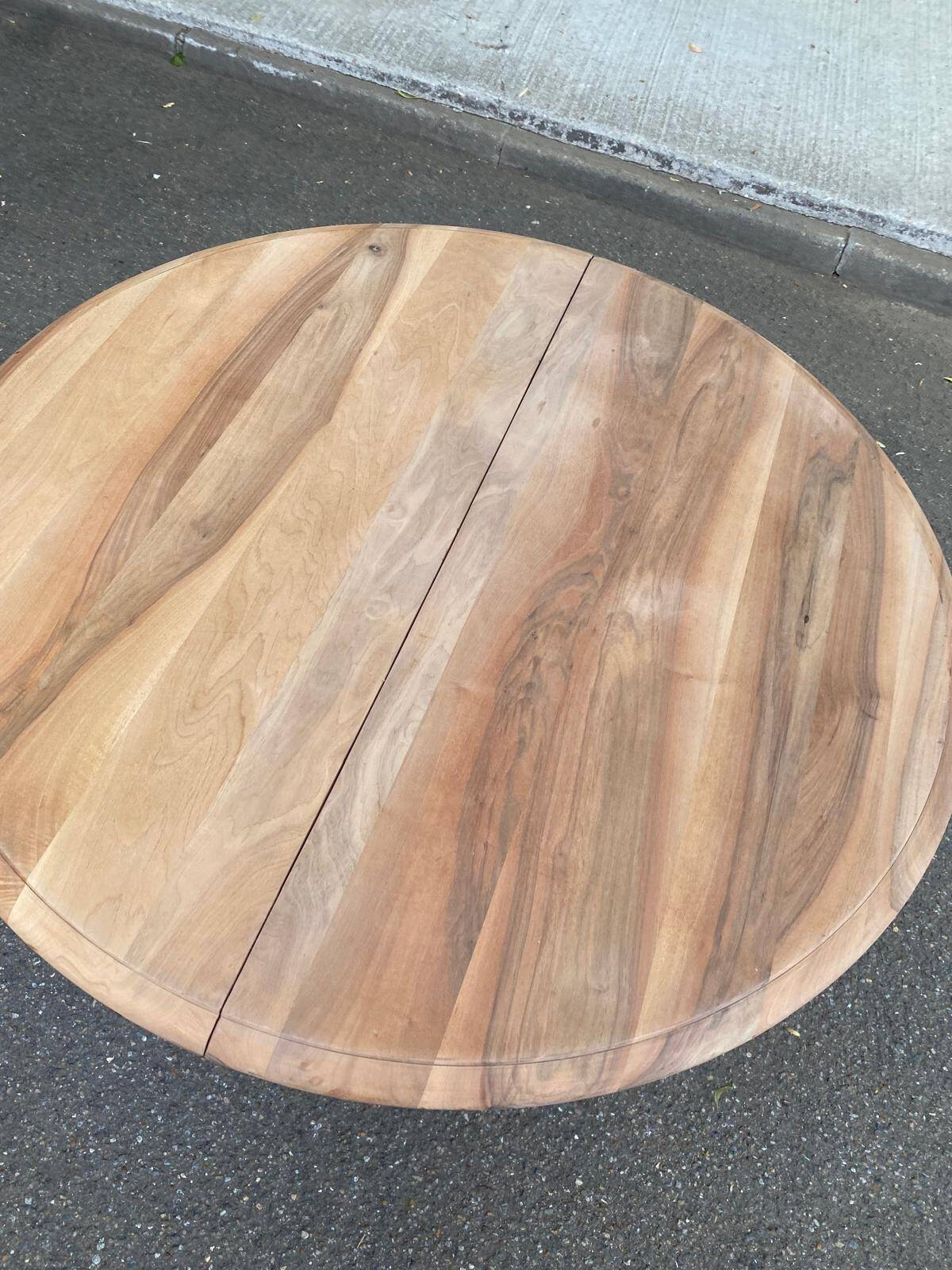 Round extendable dining table stripped in solid raw walnut with a central leg.