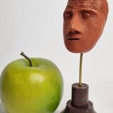Stylized head in patinated ochre terracotta on a dark wooden base, 17 cm