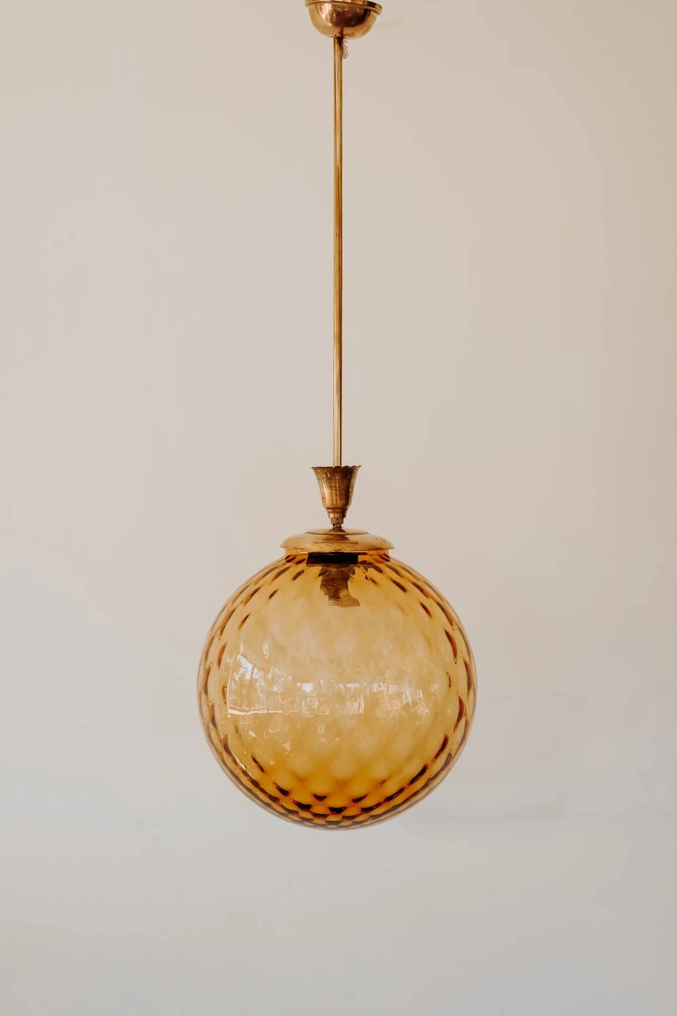 Brass pendant light with a round orange glass shade and a swirling structure.