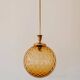 Brass pendant light with a round orange glass shade and a swirling structure.