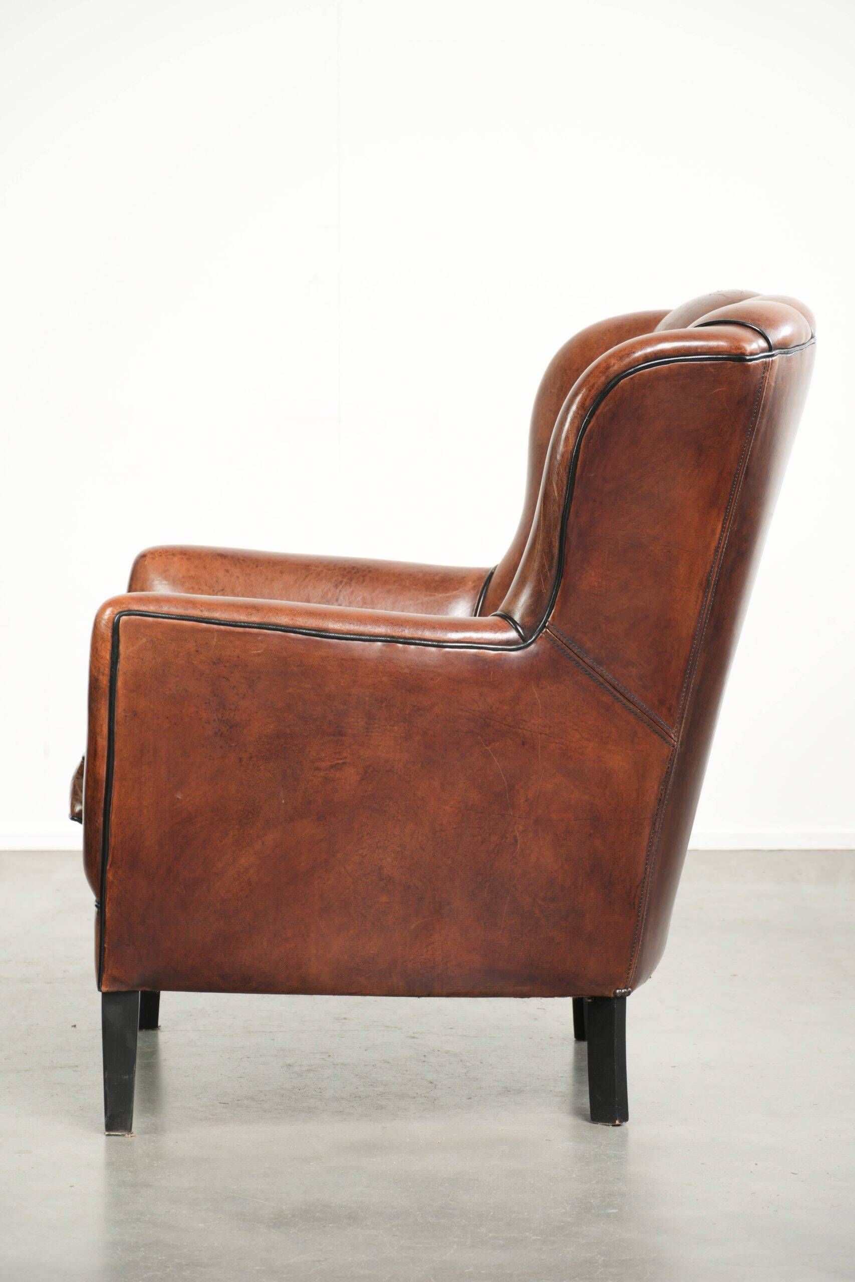 Fauteuil en peau de mouton confortable au design unique, fini avec un passepoil noir.