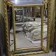 Rectangular glass with a golden frame and a pediment adorned with laurel branches.