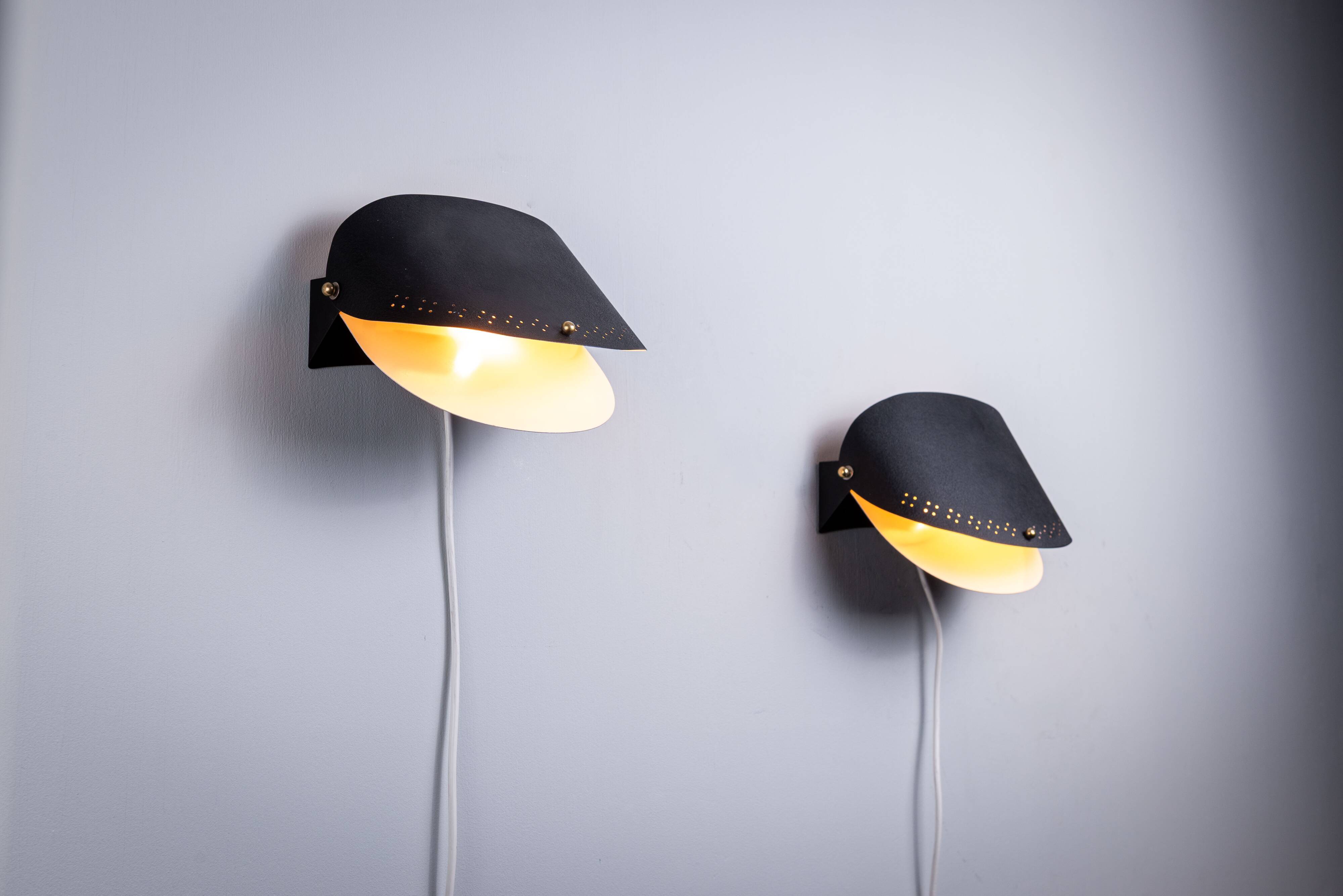 Matte black wall lamps with perforated shades and brass details