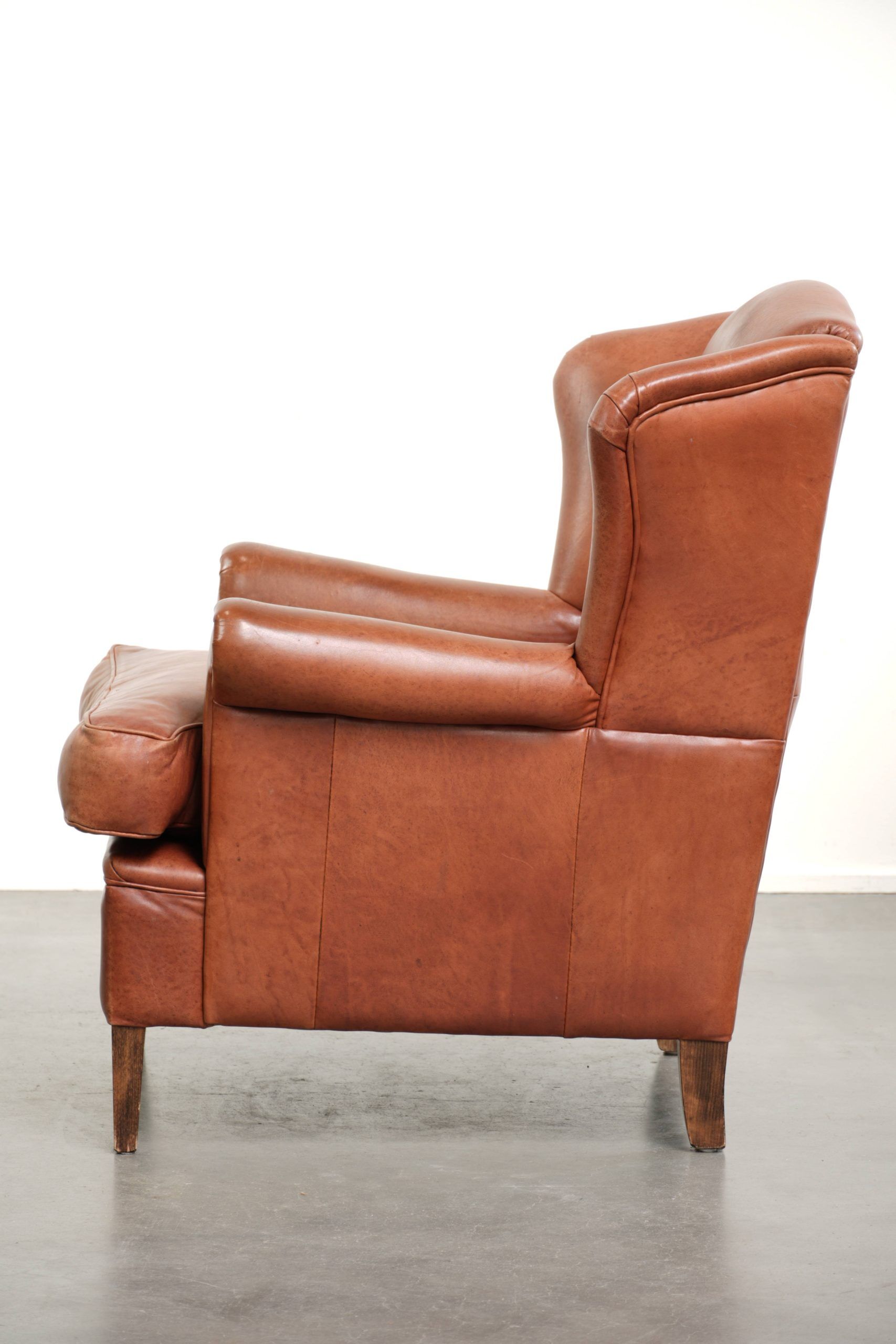 Light cognac-coloured cow leather wingback armchair with matching piping